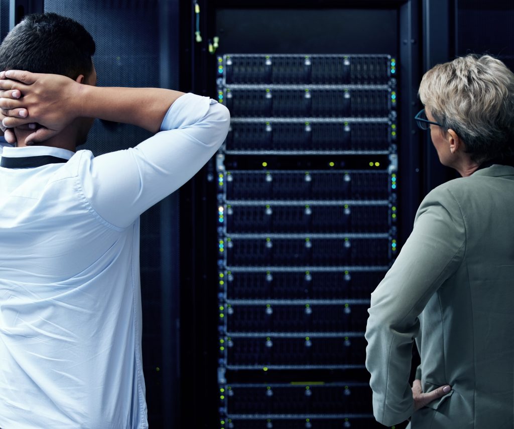 Rearview shot of two technicians looking stressed while providing emergency IT services in a data centre resolving IT crisis incident