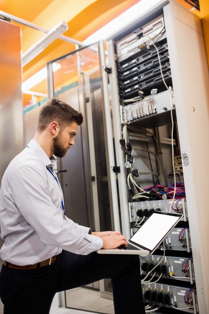 IT technician using a laptop while analyzing office server to showcase office network setup services